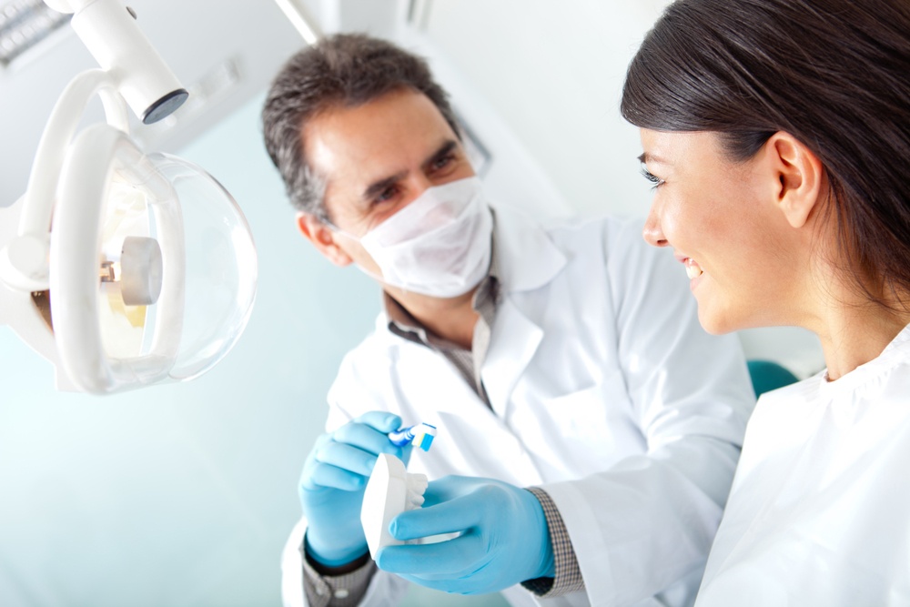 Dentist showing a woman how to brush her teeth on prosthesis.jpeg